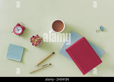 Business or office still life with open notebook or journal on a pale green background with pen, pencil, flower, mug of coffee and paper clip in an ov Stock Photo