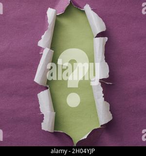 Ripped purple paper frame with decorative curled edges around a question mark on green card revealed behind Stock Photo