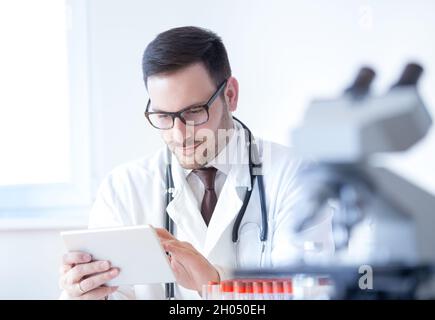 Young attractive doctor working on tablet in laboratory with blood samples and microscope Stock Photo