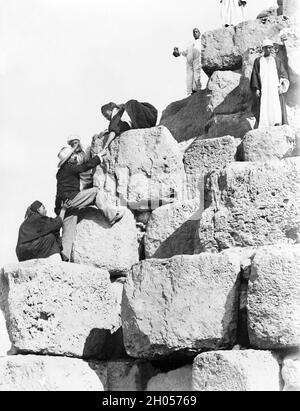 A vintage photo circa 1880 of a tourist being helped by local Egyptians to climb the Great Pyramid of Giza. Also known as the Pyramid of Khufu or the Pyramid of Cheops.   Climbing the pyramids is now banned in the present day. Stock Photo
