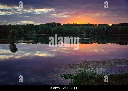 A beautiful sunset at a lake. Orange and purple clouds reflecting in the water. Long exposure. Germany, Baden-Wurttemberg. Stock Photo