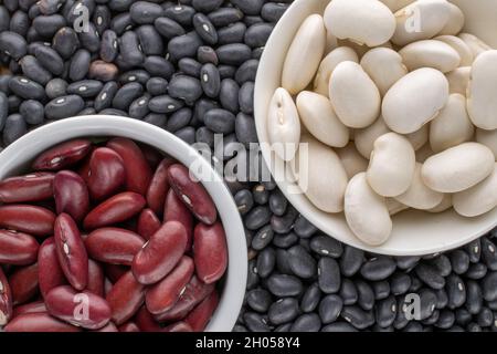 Three kinds of organic red, white, black dried beans in ceramic saucers, close-up, top view. Stock Photo