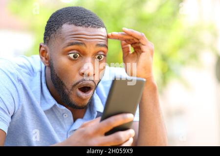 Amazed black man checking smart phone surprising content in a park Stock Photo