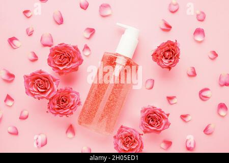 Dispenser bottle of pink shower gel or soap, and pink rose flowers on a pink background. SPA concept. Flat lay Stock Photo