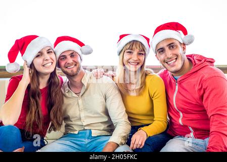 merry christmas! Young group of friends close up portrait celebrating xmas time wearing santa claus hat sitting on a couch. family time, joy, together Stock Photo