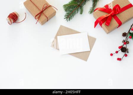 Christmas composition. Blank greeting card, envelope mockup.Decoration with christmas gifts with red bow, red berries, ribbon, fir tree branches and p Stock Photo