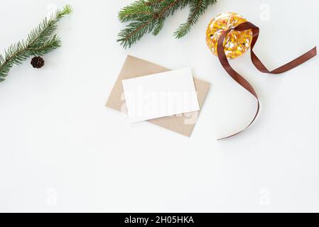 Christmas composition. Blank greeting card, envelope mockup.Decoration with Christmas glass sphere, brown ribbon, fir tree branches and pine cones on Stock Photo