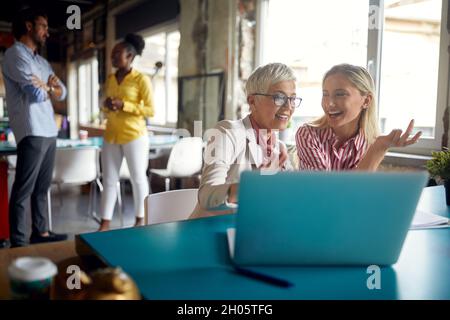 Female colleagues are commenting  and enjoying laptop content at the work in a friendly atmosphere in the office Stock Photo