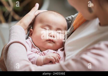 Close-up of mother holding her sleeping baby cradling her and stroking on the head Stock Photo