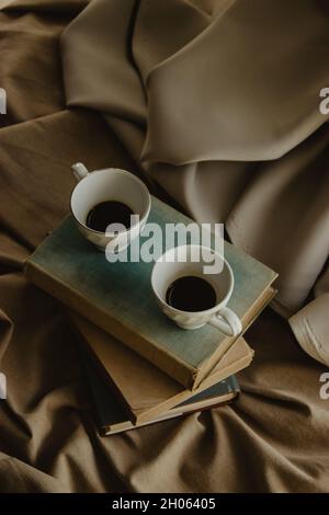 Two coffee cups on top of books on an isolated beige background. Stock Photo