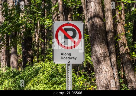 A no parking sign symbol with added words of along roadway signage on a post in the park along the forest closeup view Stock Photo