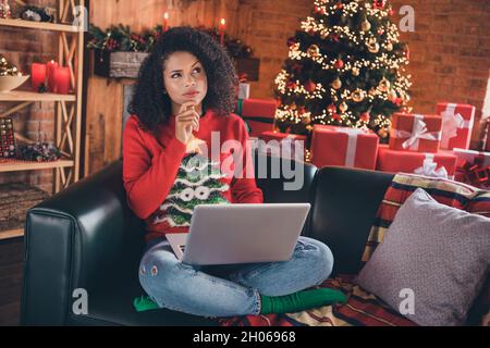 Photo of funny unsure dark skin lady wear red pullover typing modern device arms chin thinking indoors room home house Stock Photo
