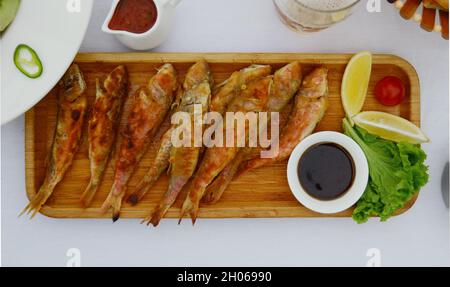 Fried red mullet on a wooden plate on a white table. Top view. Stock Photo