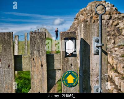 A distant runner approaches a gate marked with footpath signs on the Hadrian's Wall Path National Trail in Northumberland, UK. Taken on a sunny day wi Stock Photo