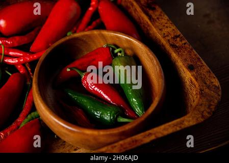 A scattering bunch of red chilies and green Romano peppers on a wooden tray. Colorful juicy hot peppers. Shot from above. Organic raw peppers. Stock Photo
