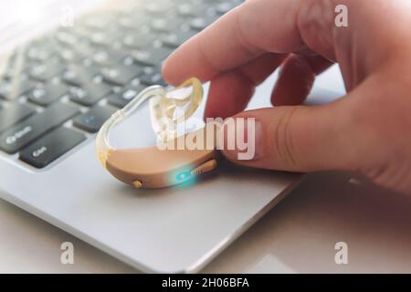 Woman's hand reaches for a hearing air on laptop Stock Photo