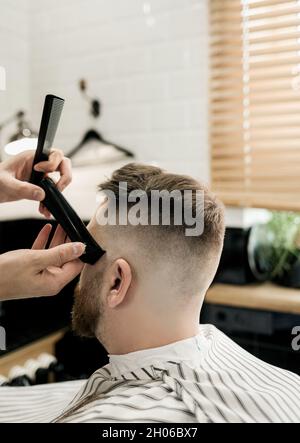 hairdresser cuts a bearded man. Work of the master in men's haircut in a barbershop. Stock Photo