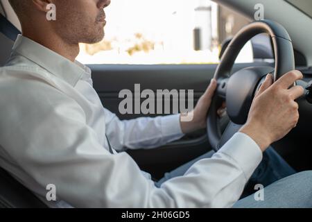 Hands of young elegant man in white shirt holding by steering wheel while driving car Stock Photo