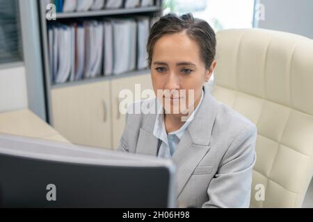 Young serious businesswoman looking at computer screen while sitting in armchair Stock Photo