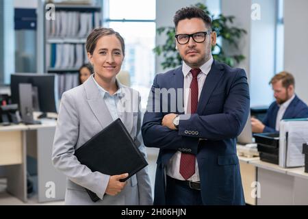 Two well-dressed employees standing in front of camera in office environment Stock Photo