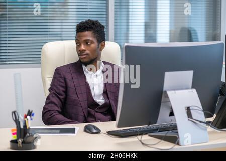 Young African businessman in formalwear looking aside while sitting in armchair by his workplace Stock Photo