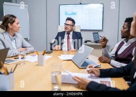 Large group of intercultural colleagues listening to explanations of confident mature business coach Stock Photo