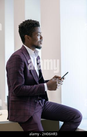 Distracted African businessman in suit scrolling in smartphone in front of camera Stock Photo
