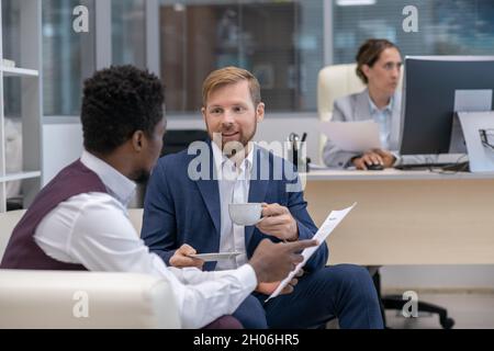 Two young intercultural office workers in suits discussing financial papers Stock Photo