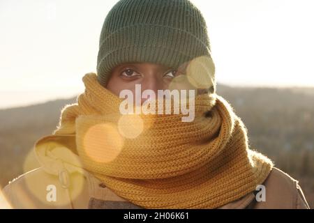 Frozen young man of African ethnicity in knitted scarf and cap looking at camera Stock Photo