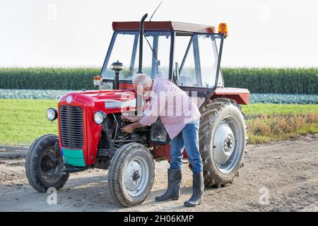 Senior farmer repairing tractor on dirt road in field Stock Photo