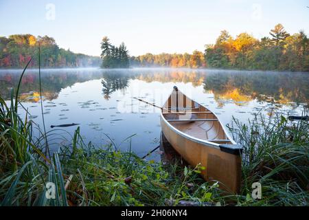 Yellow canoe on shore of calm lake with island at sunrise during autumn Stock Photo