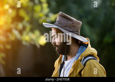Hiker with beard wearing yellow raincoat and hat and walking in forest Stock Photo