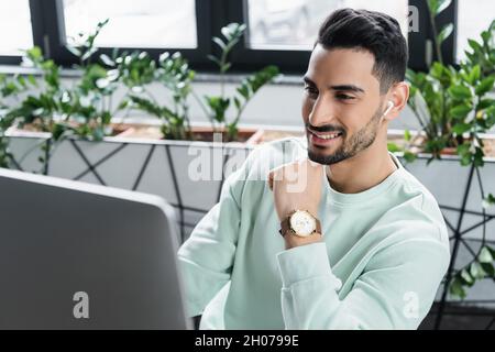 Positive arabian businessman in wireless earphone using blurred computer Stock Photo