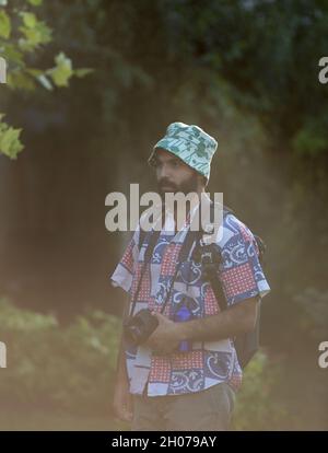 Young man with backpack walking in forest and holding camera Stock Photo