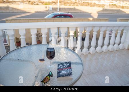 Post COVID 19 travel concept. Table outside a Spanish villa with a glass of red wine, sunglasses and a book titled Lockdown Stock Photo