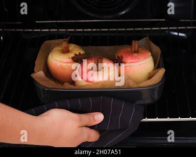 Woman taking baked apples with cinnamon and star anise in them out of an oven. Close up. Stock Photo
