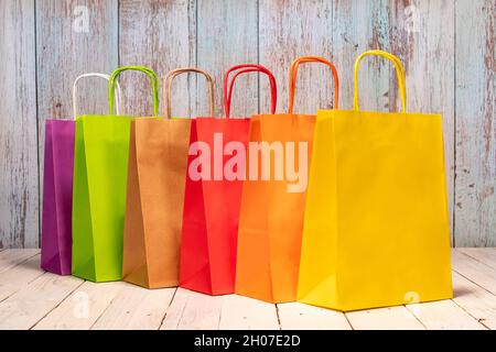 A rainbow of colorful paper bags on a shabby chic wooden table for your joyful shopping. Space for logo or a script on the yellow bag. Stock Photo