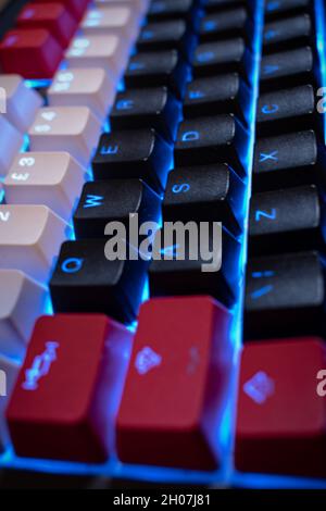 Blue Backlit Mechanical Keyboard with black, white, red keycaps at an angle Stock Photo