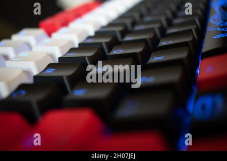 Blue Backlit Mechanical Keyboard with black, white, red keycaps at an angle Stock Photo