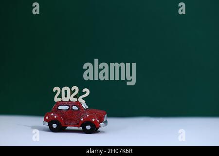 A red car with the numbers 2022 on the roof carries New Year's gifts. New Year in the car showroom. Stock Photo