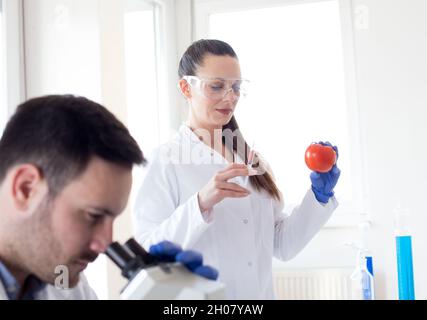 Two scientists doing  research with vegetables in lab with microscope Stock Photo