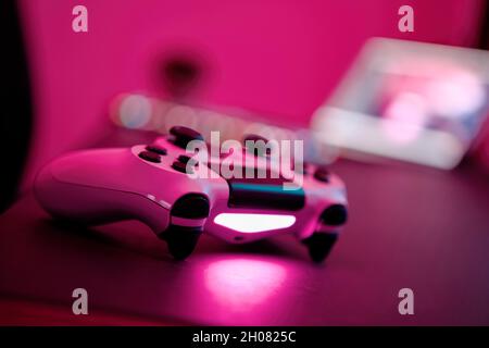 Close-up of gaming controller laying on table in purple illuminated room. Selective focus. Professional computer game playing, esport business and onl Stock Photo