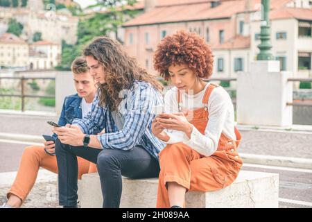 Multicultural group of friends using mobile phones - Students sitting in a row and typing on smartphones Stock Photo