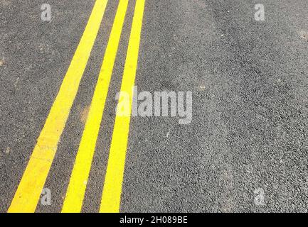 Three yellow lines in dark tarmac road with space for copy Stock Photo