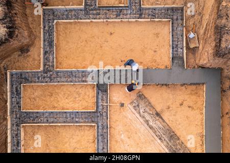 Workers leveling poured liquid concrete or cement on steel reinforcement, building foundation construction in process, aerial top view. Stock Photo