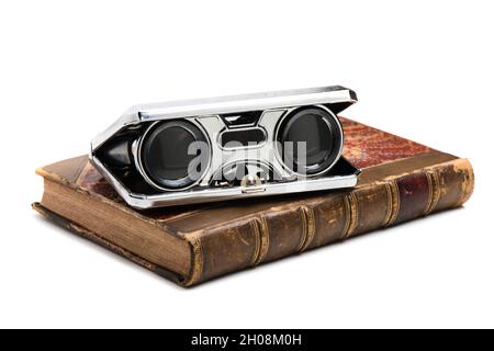 closeup vintage folding opera glasses on an old book. Old compact binoculars. Stock Photo