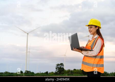 young female engineer working with laptop computer against wind turbine farm Stock Photo