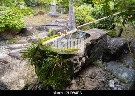 Large stone water basin with bamboo pipe and running water. Japanese garden motif. Stock Photo