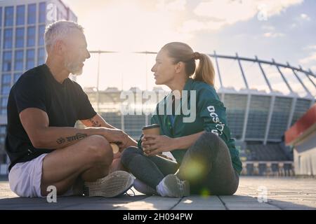 Attractive mature couple communicating with each other while resting outdoors after morning workout on a sunny summer day Stock Photo