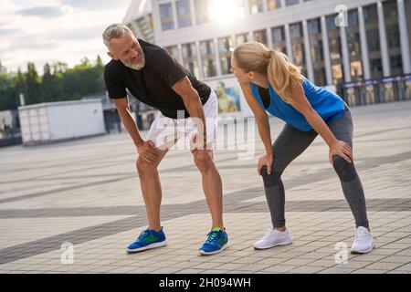Mature couple, man and woman looking at each other, taking a short break while jogging together in the city on a warm summer day Stock Photo